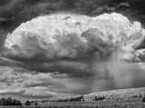 Black and white photograph of a dramatic storm cloud releasing rain over a vast Wyoming landscape.
