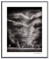 A silver-framed black and white photograph of dramatic, swirling clouds over a rural California farm.
