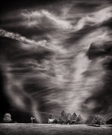 Soft, dancing cloud formations revealed against the darkened sky of a black and white landscape photograph.