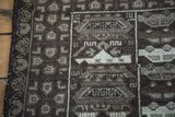 Stylized brown and beige vehicle motifs and geometric patterns on vintage Afghan war rug.