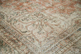 Distressed Oushak rug corner featuring blanched terra cotta, silver, and ivory patterns.