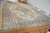 Blanched beige vintage Oushak carpet corner showcasing muted blue floral details and fringe.