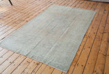 Distressed vintage Oushak carpet showing muted beige and slate green patterns.