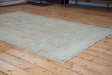 Distressed Oushak carpet edge, highlighting faded beige and soft slate green patterns.