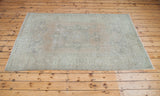 Distressed Oushak rug corner, showing faded floral patterns in soft beige and slate green.