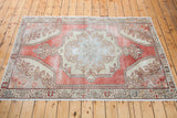 Distressed cranberry red and ivory curvilinear motifs on a vintage Oushak rug corner.