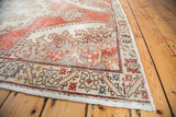 Distressed vintage Oushak rug corner with soft cranberry field, intricate border, and fringe.