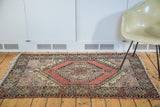 Vintage Turkish Oushak rug corner displaying geometric patterns in brick red, beige, and muted gray with fringe.
