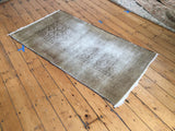 Distressed Belouch rug with a faded light brown pile and faint serrated leaf pattern.