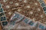 Vintage Oushak rug folded, revealing brown lattice pile and muted blue woven reverse foundation.