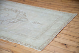 Faded bronze interlocking border detail on the blanched Oushak rug's natural edge.
