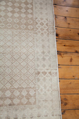 Distressed harlequin diamond pattern detail on a vintage rug with softened beige and ivory tones.