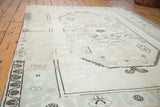 Faded ivory and blanched Oushak rug with abstract charcoal motifs and patterned border.