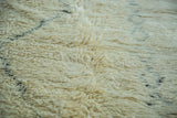 Plush pale ivory pile of a vintage Moroccan rug, revealing blanched charcoal outlines.