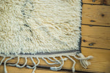 Plush pale ivory pile, blanched charcoal outlines, and braided fringe of a vintage Moroccan rug.