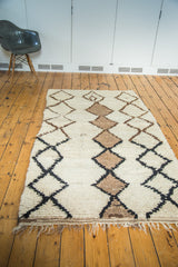 Textured pile and fringed edge of vintage Moroccan rug with ivory, grey, charcoal black lattice.