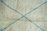 Close-up: shaggy ivory vintage Moroccan carpet with intersecting chalk-sky blue lines.
