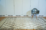 Textured corner of a vintage Moroccan carpet, revealing its shaggy ivory pile and charcoal lattice pattern.