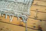Thick shaggy pile texture in blanched ivory and charcoal grey with braided fringe.