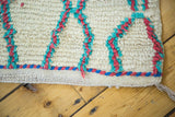 Textured ivory Moroccan rug pile with hot pink, aqua blue lattice and braided red, blue edge.