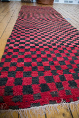 Vintage Moroccan rug's textured red and charcoal checkered pattern, with white fringe.