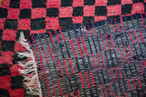 Moroccan rug with thick red and black checkered pile, woven striped back, and fringe.