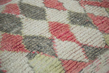 Moroccan rug's textured pile: faded harlequin diamonds in red grapefruit, silvery grey, ivory.