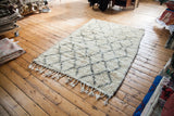 Fluffy ivory pile of vintage Beni Ourain Moroccan rug with charcoal lattice and tassels.