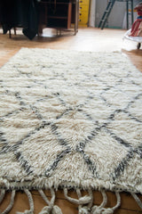 Fluffy ivory pile with charcoal lattice pattern and braided fringe on a Beni Ourain Moroccan carpet.