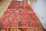 Textured cherry red vintage Moroccan rug end, displaying blue and yellow lattice and fringe.