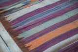 Geometric striped kilim detail in purple, orange, ivory, gray, and bronze tones.
