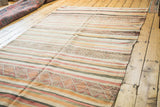 Vintage tribal kilim runner, geometric motifs amidst stripes in ivory, red, and orange.