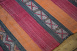 Serrated geometric patterns on charcoal, orange, and reddish-pink kilim stripes.