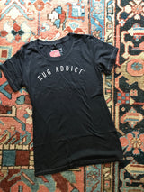 Women's charcoal scoop neck t-shirt with white 'Rug Addict' text and contrast stitching.