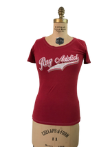 Women's scoop neck t-shirt in watermelon red with a retro layered Rug Addict script graphic.