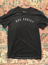 Men's charcoal Rug Addict t-shirt with arched white letters and contrast stitching.
