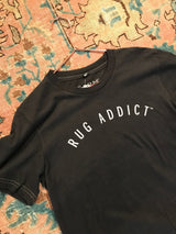 Charcoal Rug Addict t-shirt from an angle showing arched text and contrast stitching.
