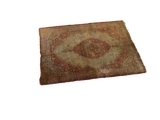 Angled view of an antique silk Tabriz mat showcasing its medallion design and time-softened patina.