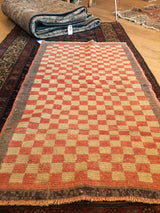 Textural close-up of the vintage Tulu rug showing stepped peach, beige, and grey checks with fringe.