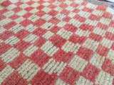 Stepped checkered pattern detail of a vintage Tulu rug, muted red and beige shaggy pile.