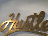 Angled close-up of the gold 'Hustle' decor sign, showing hand-painted texture and layered wood.