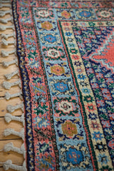 Plush, thick pile and braided fringe of a vintage Moroccan carpet in blush red and blues.