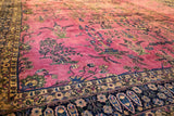 Angled view of the vintage carpet's magenta field showing cypress trees and the navy border.