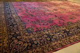 Low angle view of a vintage Meshed carpet showing its magenta floral field and intricate navy border.