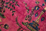 Close-up of hand-knotted floral sprays and potted plant designs on a deep magenta wool pile.