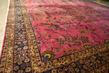 Angled perspective on a vintage Meshed carpet's cochineal red field with sprawling vines and a detailed border.