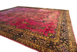 Low-angle view of a vintage Meshed carpet's rich magenta field and complex floral border.
