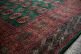 Intricate rust and navy geometric border detail on a plush emerald green vintage Bokhara carpet.