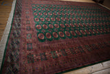 Vintage Bokhara carpet corner, displaying emerald green gul medallions and intricate rust borders.