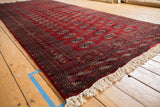 Angled view of a vintage Bokhara runner showing the sheen on its plush, cherry red wool pile.